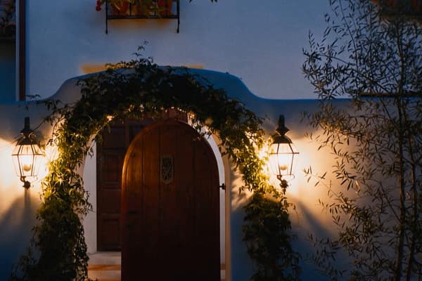An arched wooden front door in the evening, a lit lantern on each side
